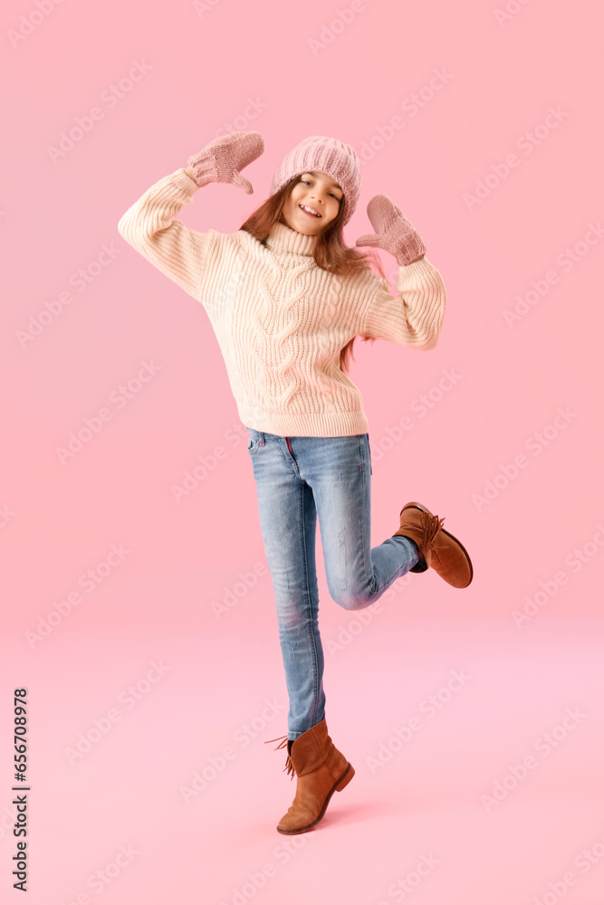 Happy little girl in winter clothes on pink background