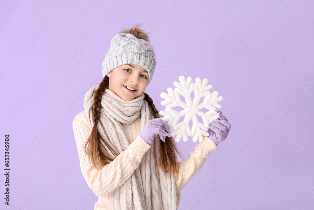 Cute little girl in winter clothes with big snowflake on lilac background
