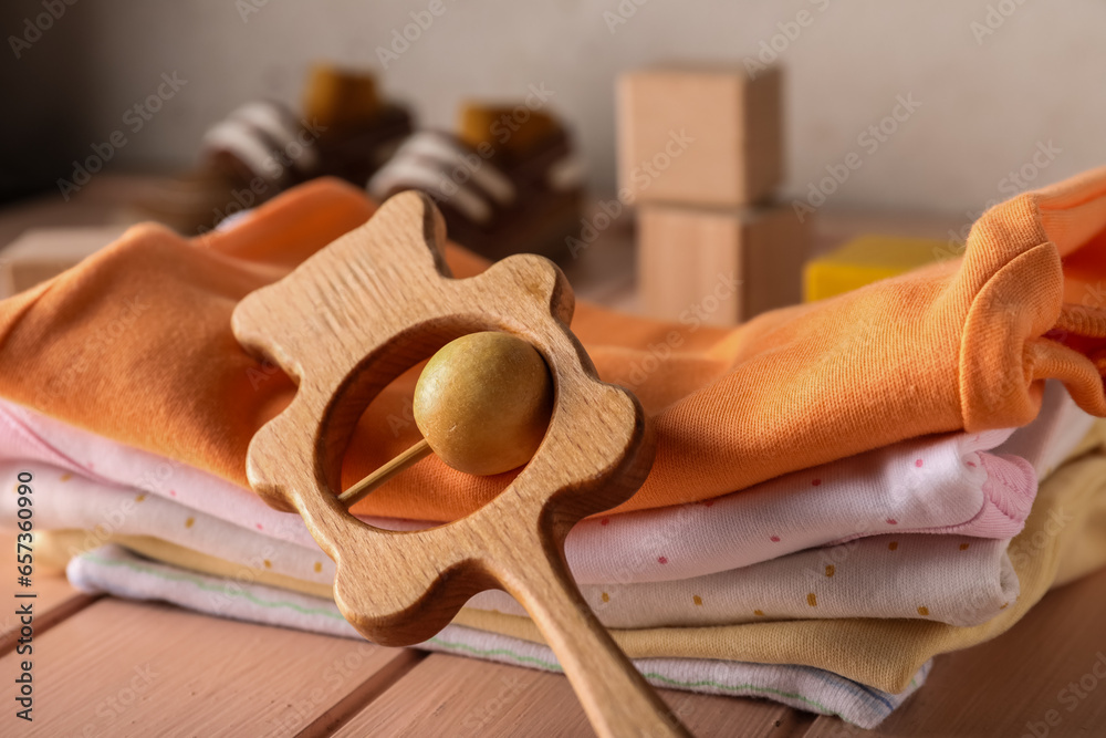 Stack of baby clothes and rattle on color wooden table, closeup
