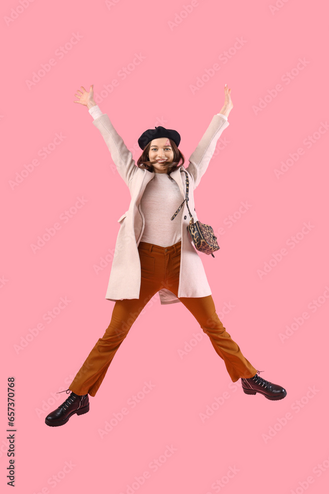 Jumping young woman in stylish autumn outfit on pink background