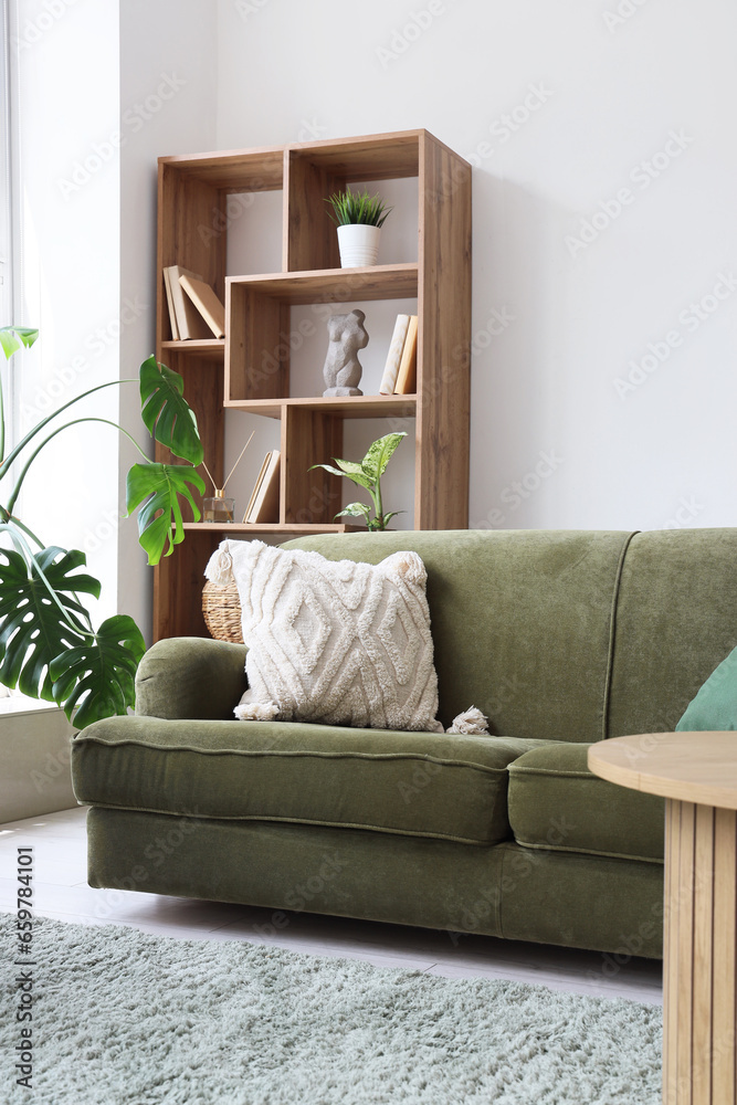 Interior of light living room with cozy green sofa, shelving unit and houseplants