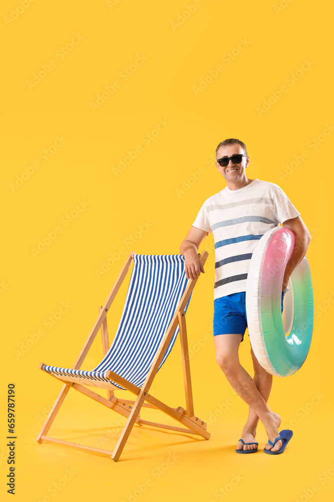 Mature man with swim ring and deck chair on yellow background