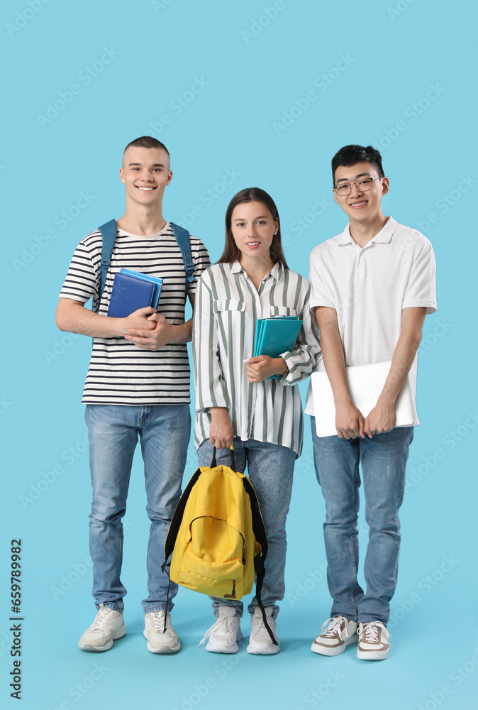 Happy students with notebooks, books and laptop on blue background
