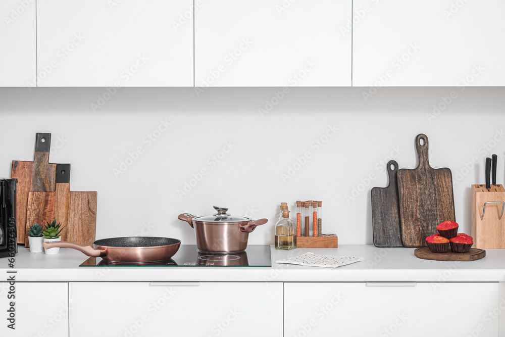 White kitchen countertop with electric stove, frying pan, cooking pot and utensils