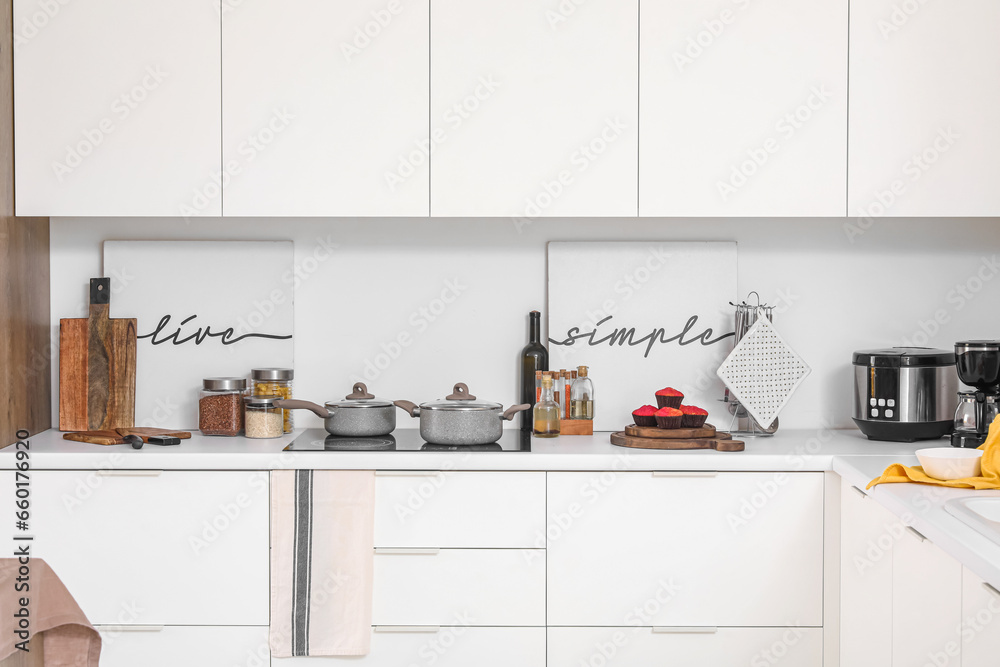 White kitchen counter with electric stove, cooking pots and utensils