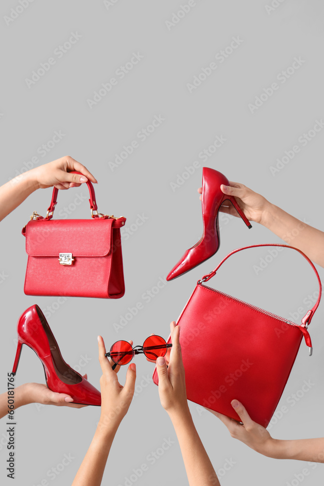 Female hands holding different stylish bags, sunglasses and high heels on grey background