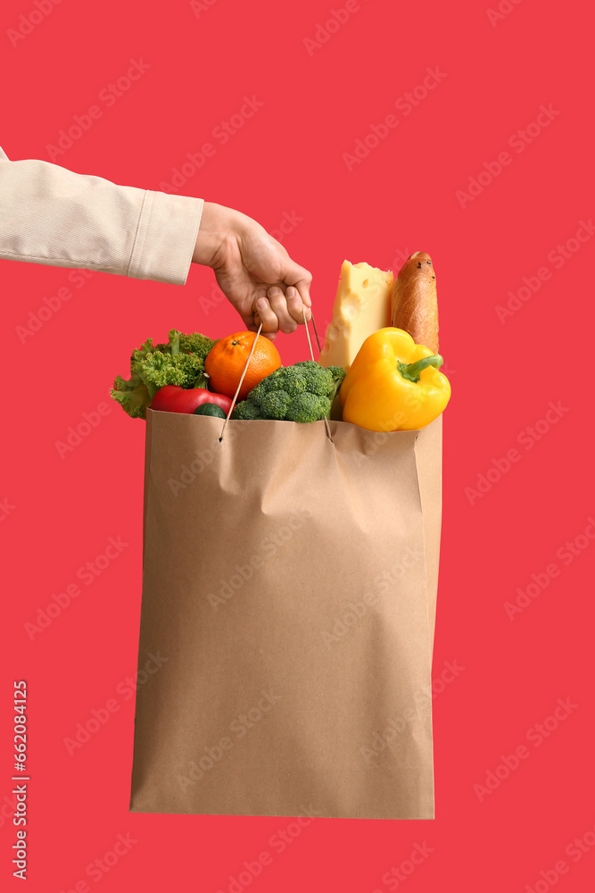 Woman holding paper bag with healthy products on red background. Food delivery service