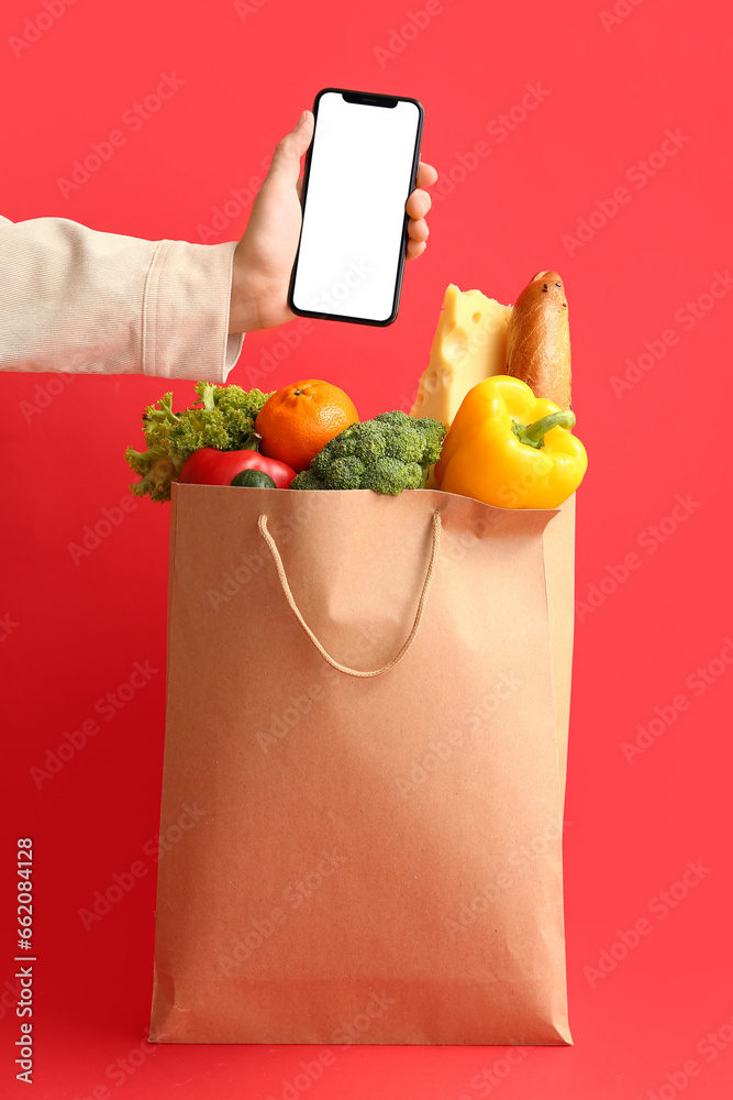 Woman holding smartphone and paper bag with food on red background
