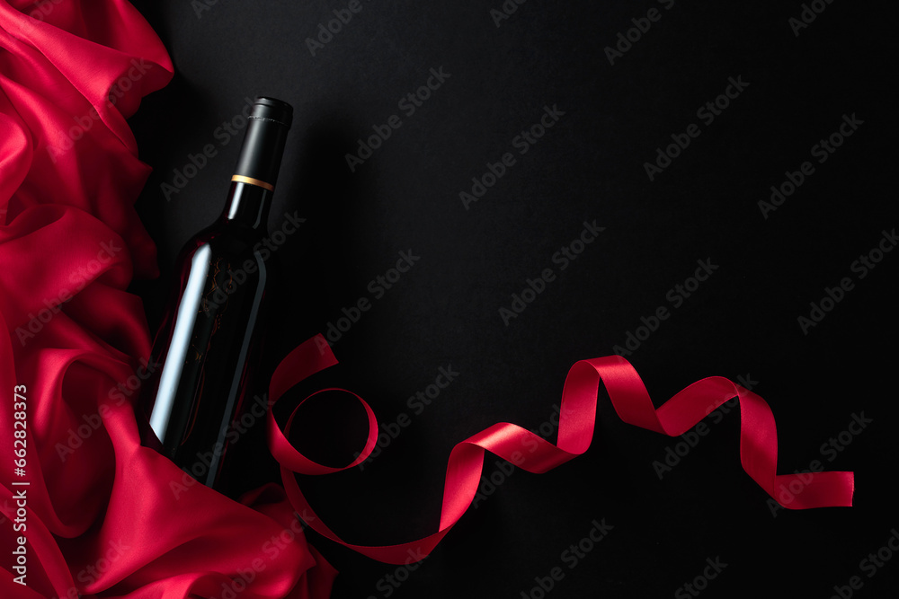 Bottle of red wine with red satin on a black background.