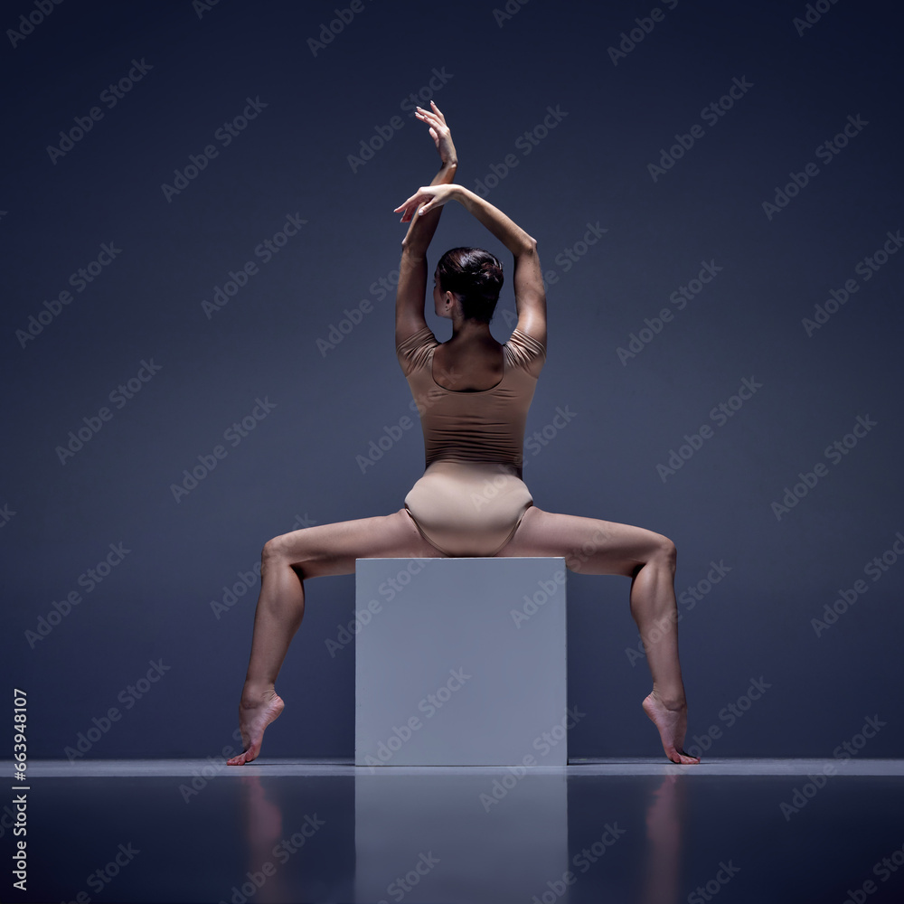 Passion. Elegant ballerina, young woman in beige bodysuit posing on cube against blue studio background. Concept of classical dance, art and grace, beauty, choreography, inspiration