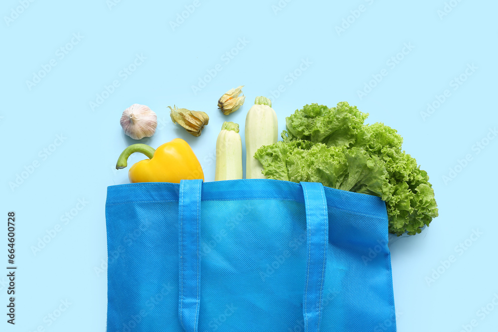 Eco bag with different fresh vegetables on blue background