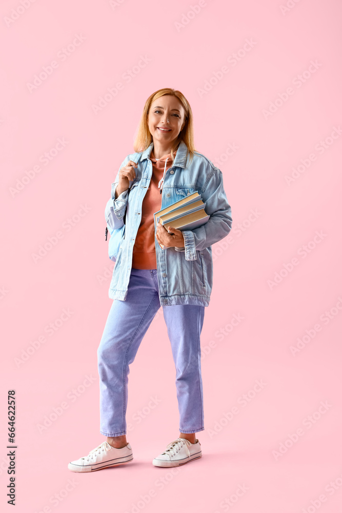 Mature woman in denim jacket with books and backpack on pink background