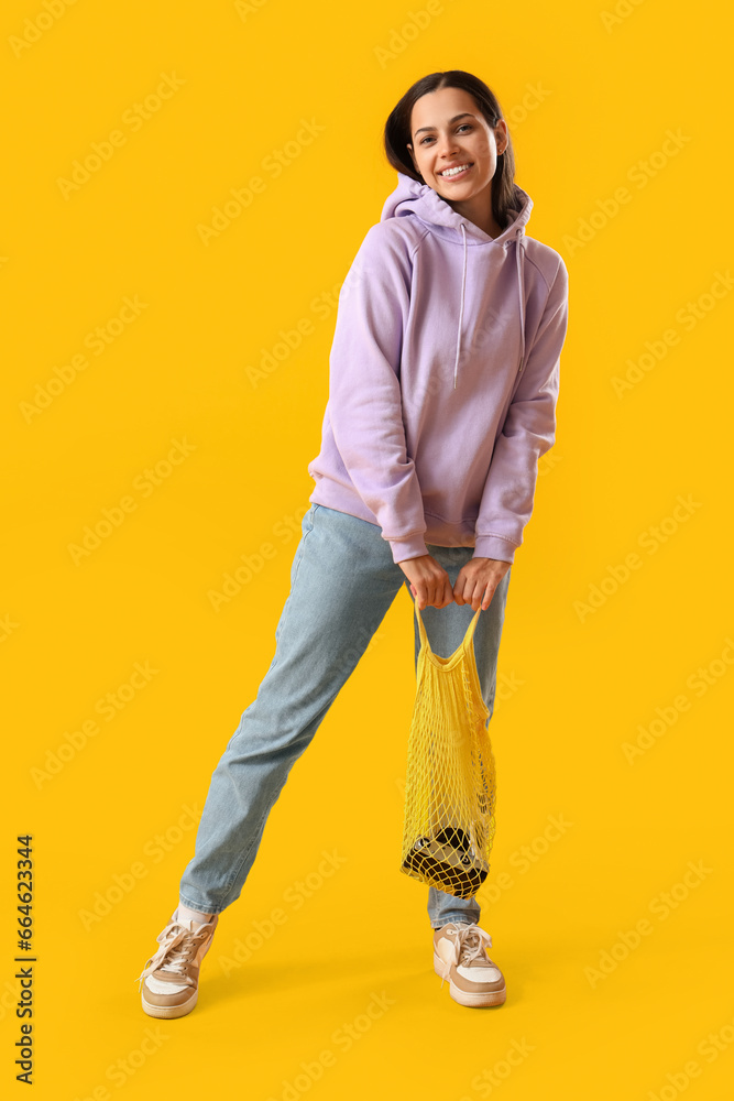 Young woman in lilac hoodie with string bag on yellow background