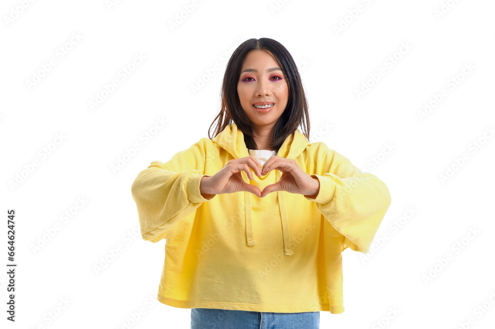 Young Asian woman in yellow hoodie making heart gesture on white background