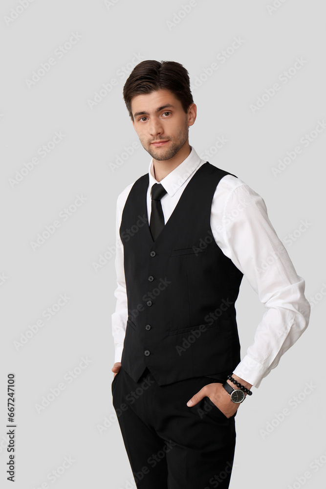 Handsome young businessman with wristwatch on grey background