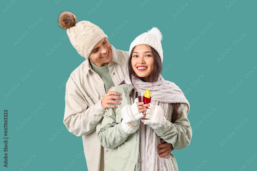 Happy couple in warm clothes with glass of tasty mulled wine on turquoise background