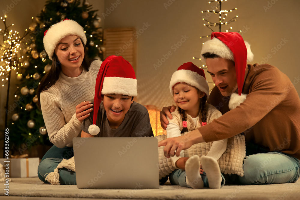 Happy family in Santa hats watching Christmas movie on laptop at home
