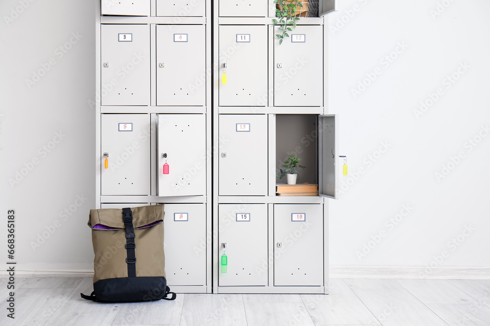 Modern locker with books, plants and backpack near light wall