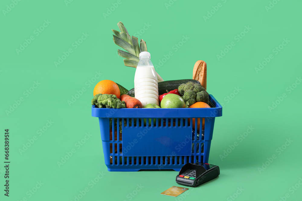 Shopping basket full of food with payment terminal and credit card on green background