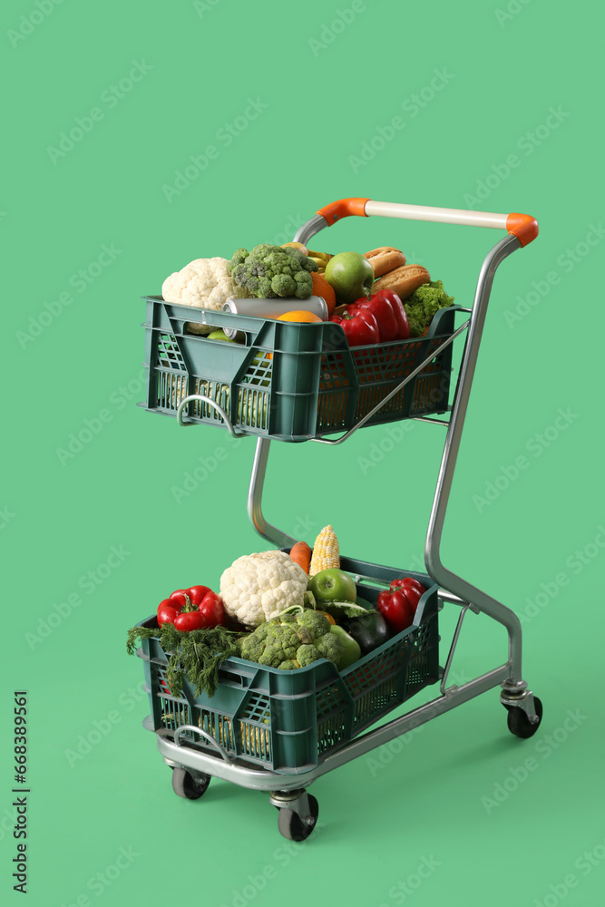 Shopping cart full of fresh vegetables on green background