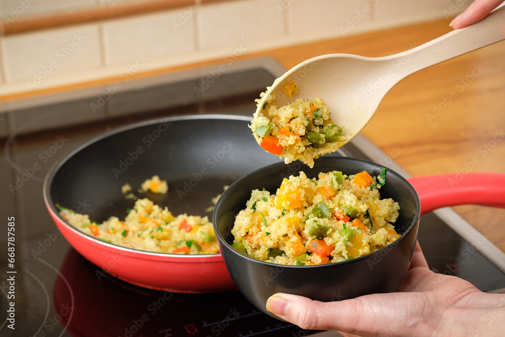 Woman puts food in a bowl from a frying pan. Cooked quinoa with vegetables - red and green bell pepper, carrot, pupkin and parsley. Healthy gluten free vegan and vegetarian food.