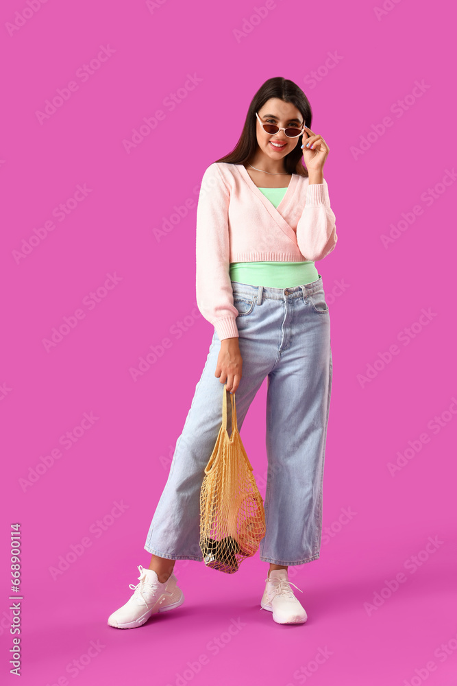 Beautiful young woman with string bag on purple background