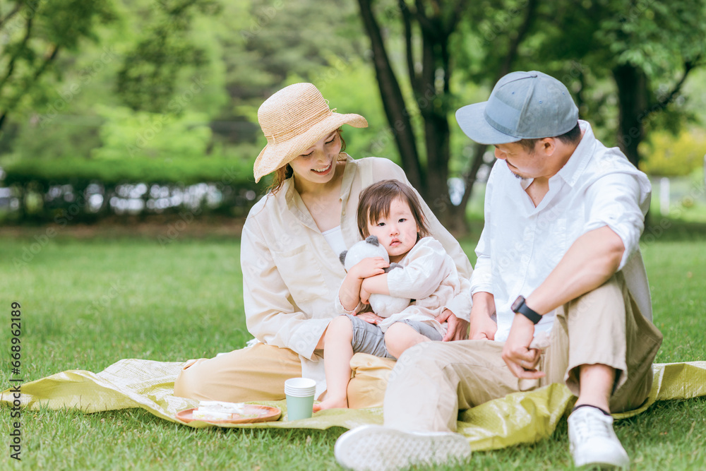 新緑の公園でピクニックする親子・家族とぬいぐるみで遊ぶ娘・女の子・子供（春・夏） 