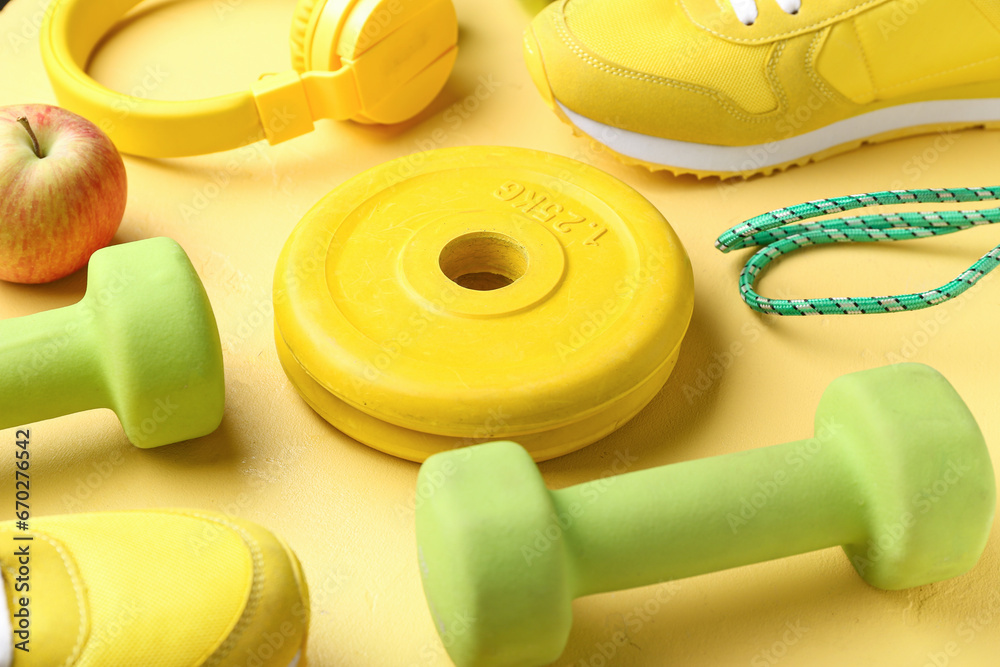 Barbell plates, shoes and dumbbells on yellow background