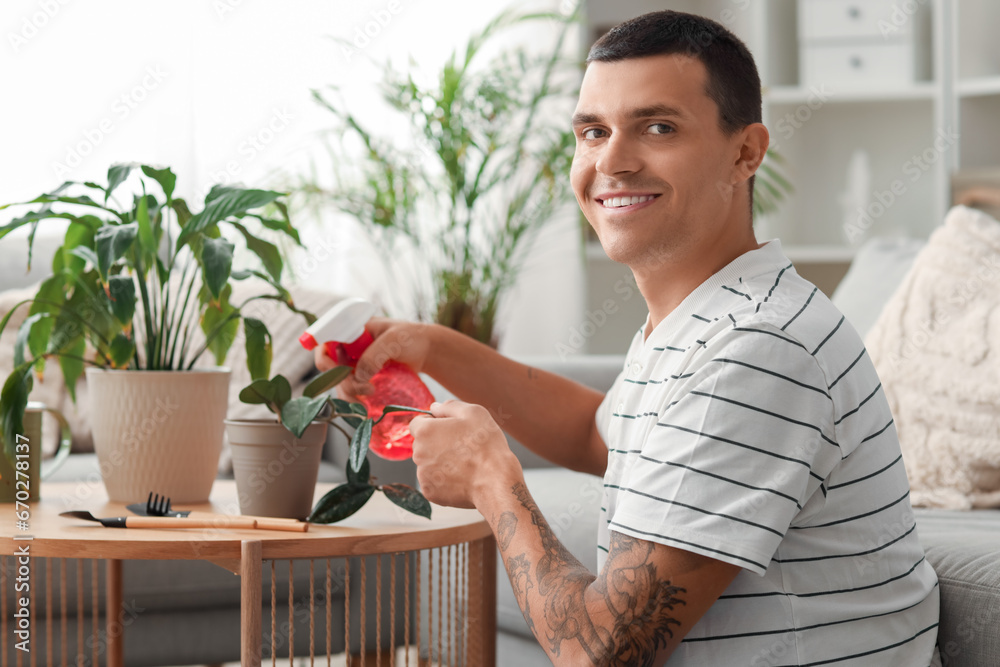 Young man watering plant at home
