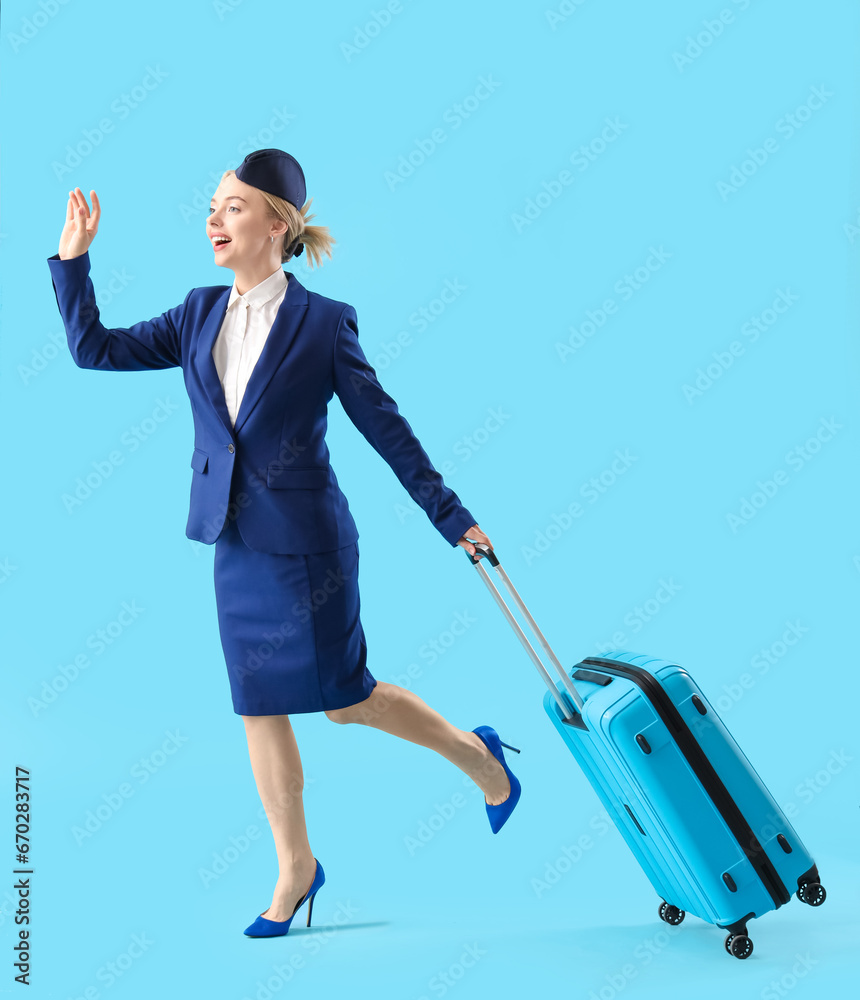 Young stewardess with suitcase on blue background