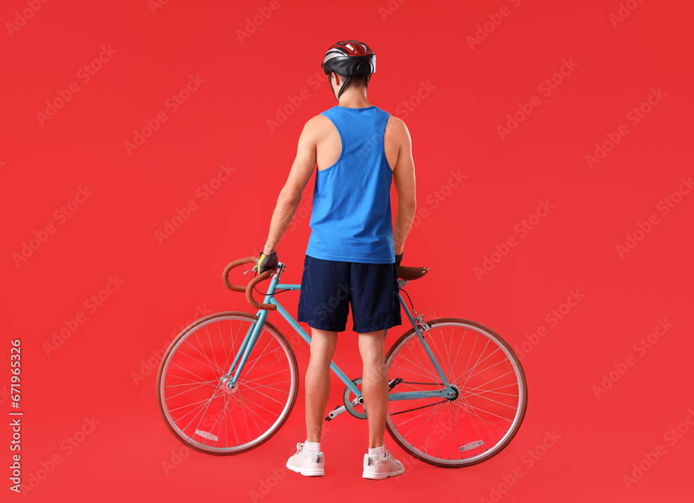 Young man with bicycle on red background, back view