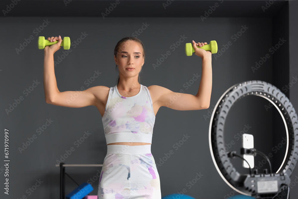 Female sports blogger with dumbbells recording video in gym