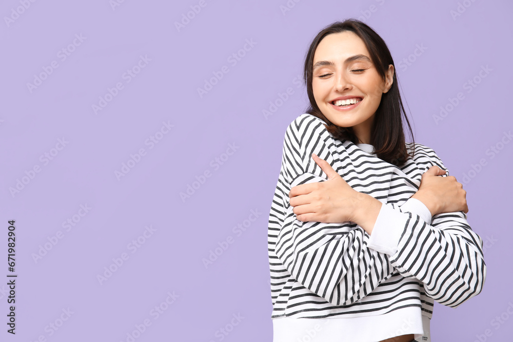 Young woman hugging herself on lilac background