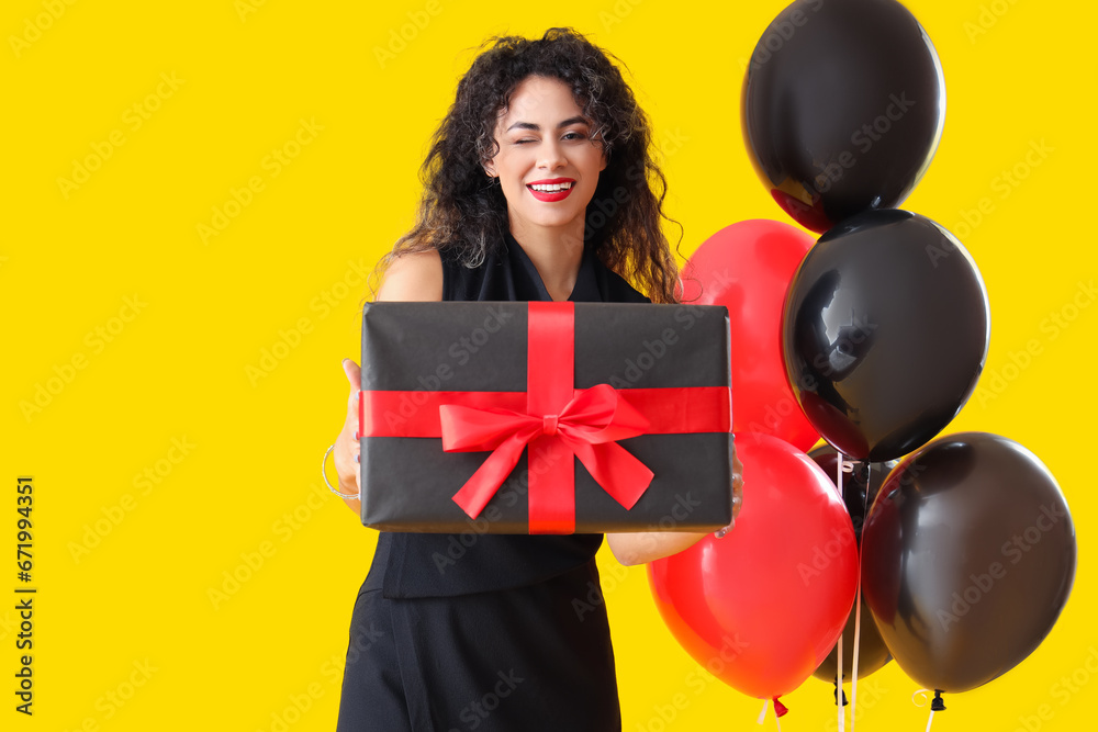 Beautiful African-American woman with gift box and balloons on yellow background. Black Friday sale