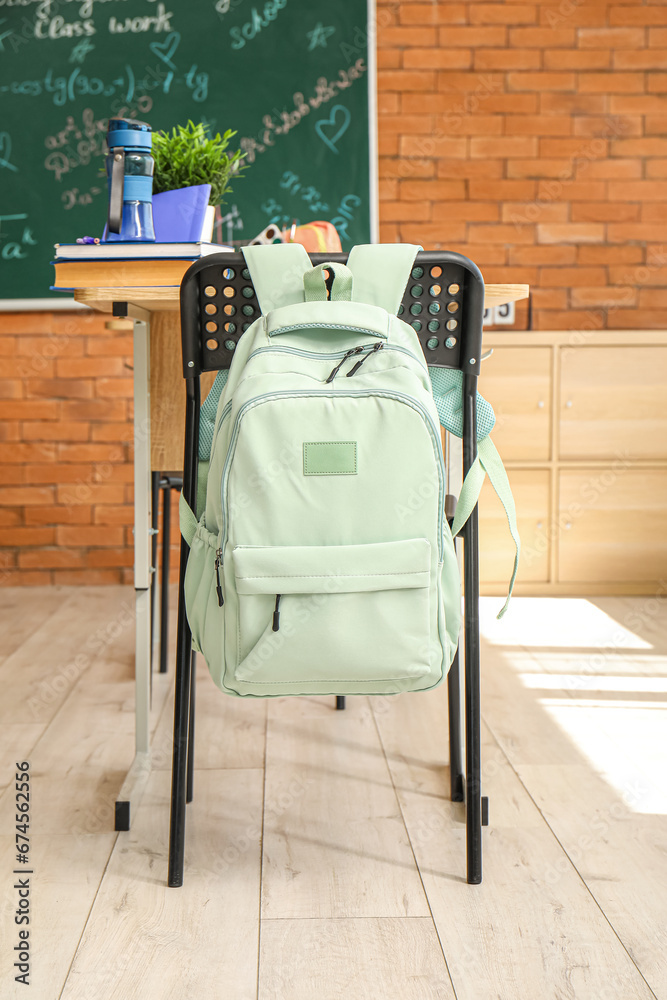 Stylish school backpack hanging on chair in classroom