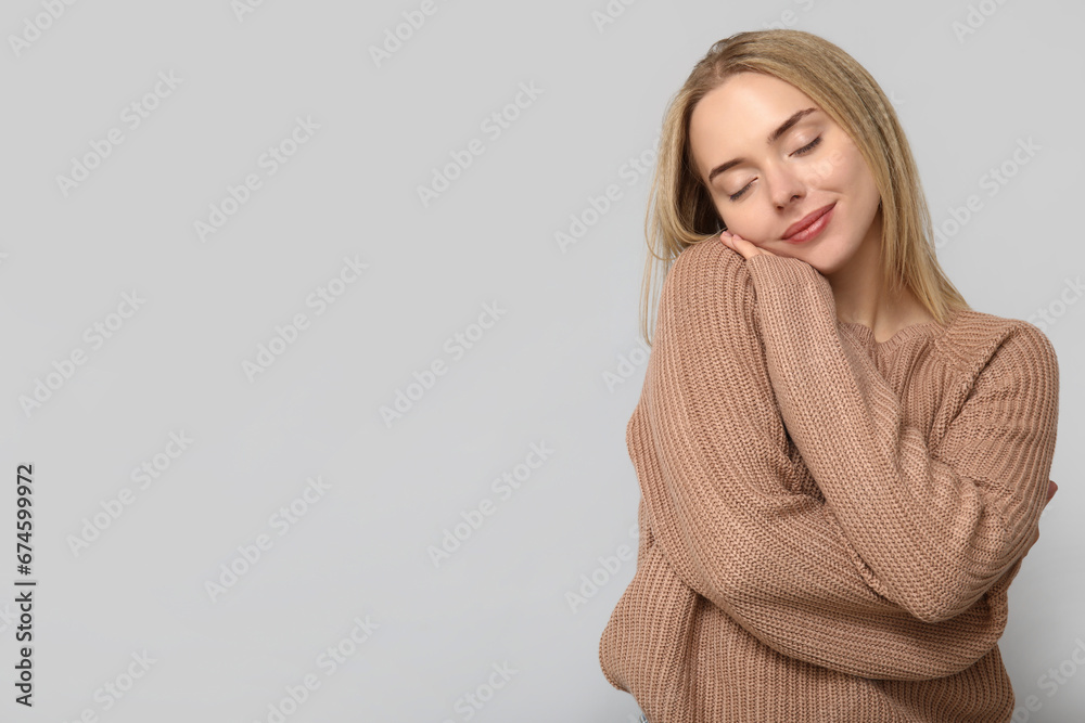 Young woman hugging herself on grey background