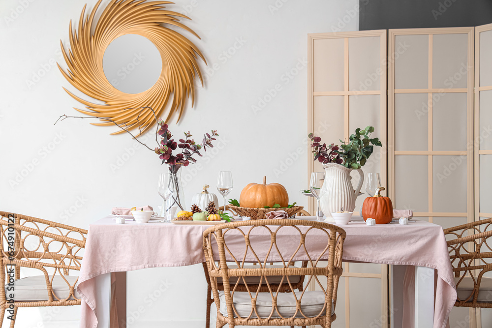 Autumn table setting decorated for Thanksgiving Day with pumpkins and eucalyptus branches in light dining room