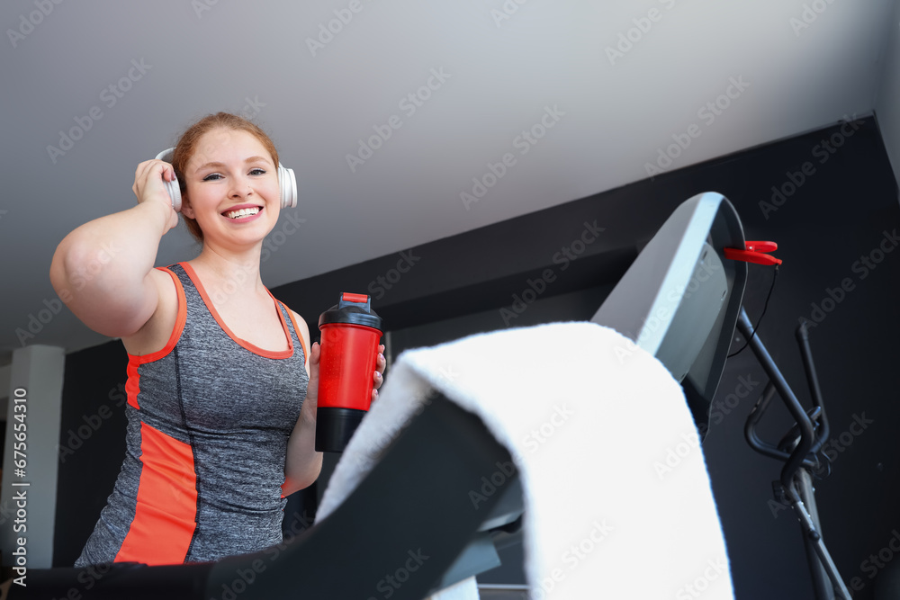 Beautiful young woman running on treadmill in gym while listening to music