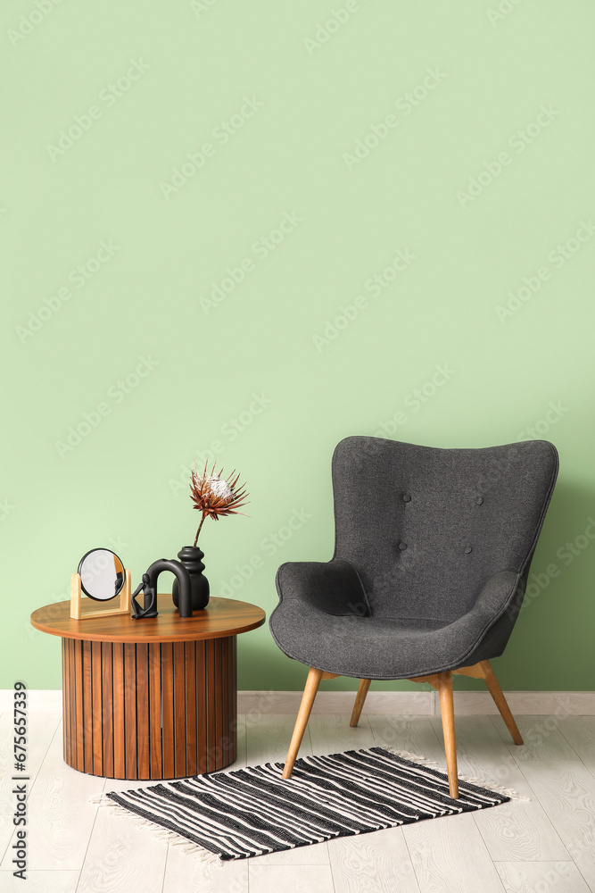 Stylish rug, grey armchair and coffee table with decor near green wall