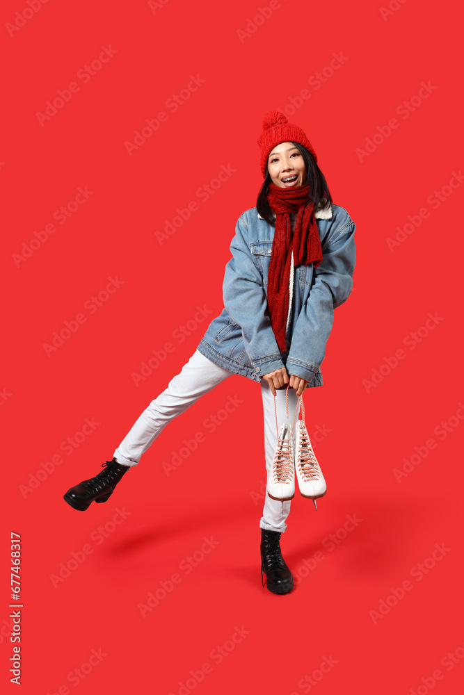 Young Asian woman in winter clothes with ice skates on red background