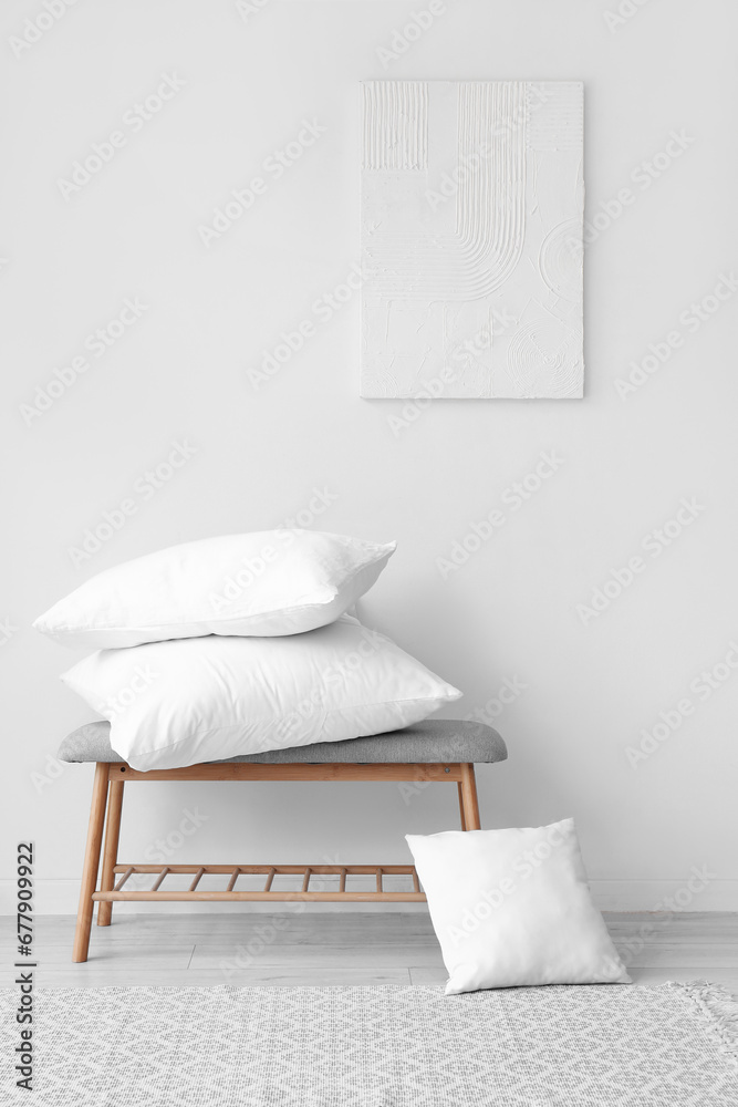 Grey bench with pillows near white wall