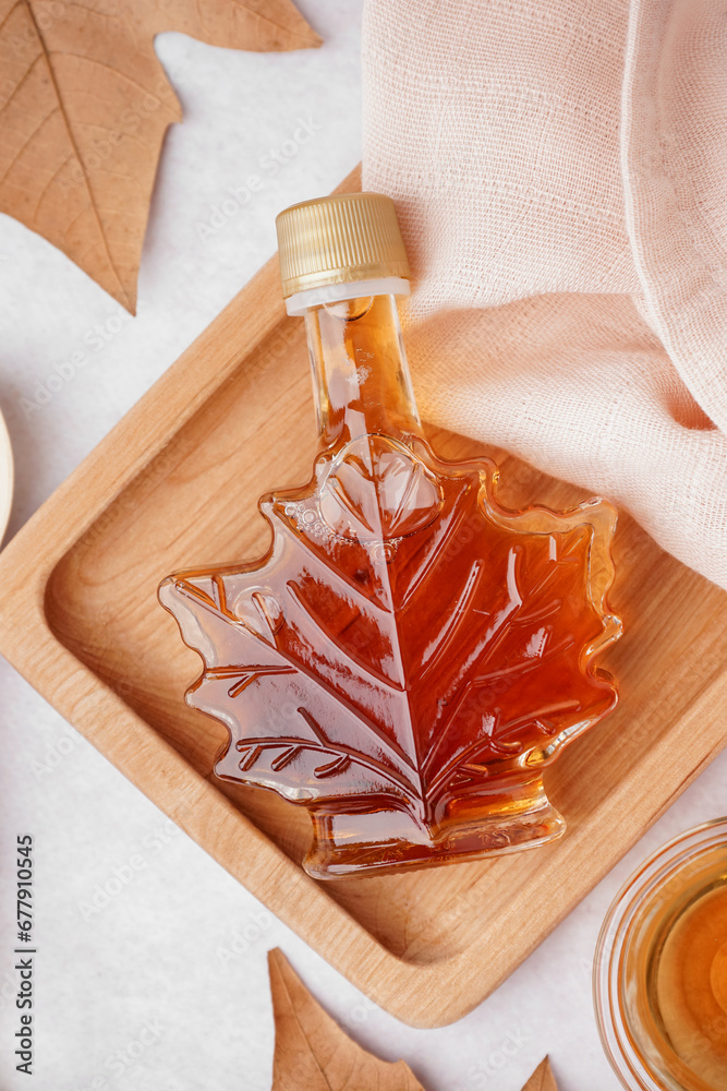 Bottle of tasty maple syrup on light background