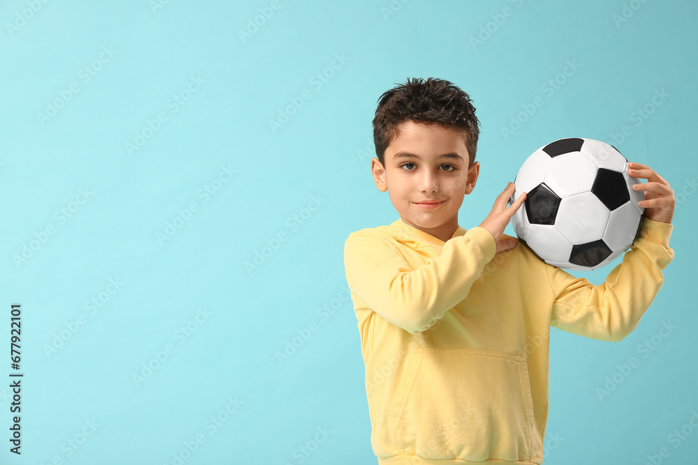Cute little boy with soccer ball on blue background