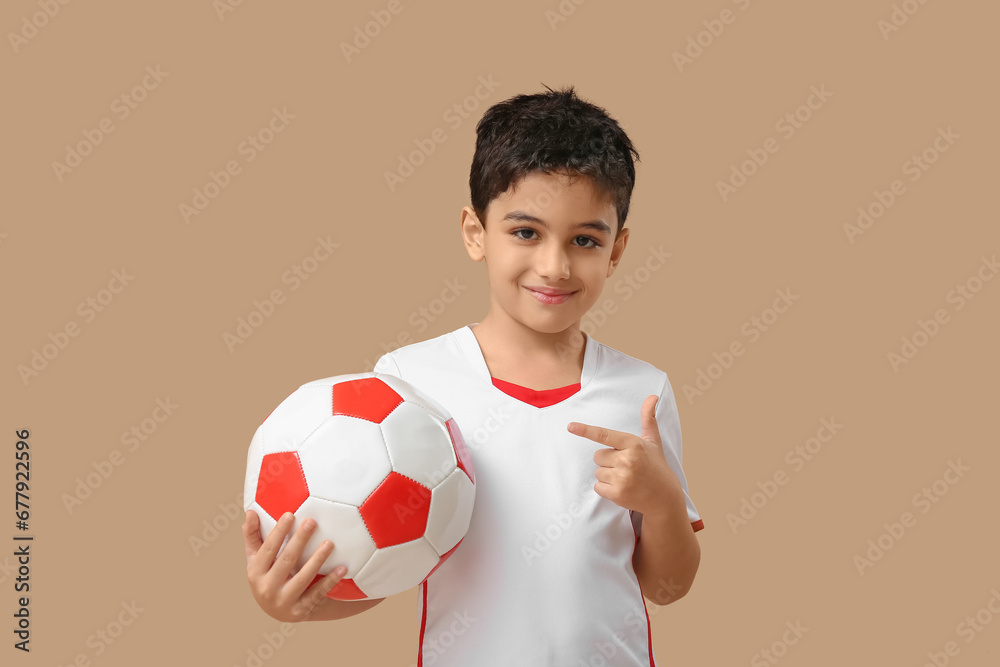 Cute little boy pointing at soccer ball on beige background