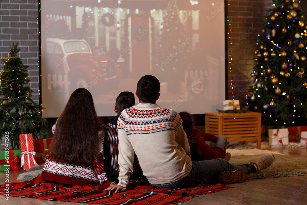 Happy family watching Christmas movie on projector screen at home, back view