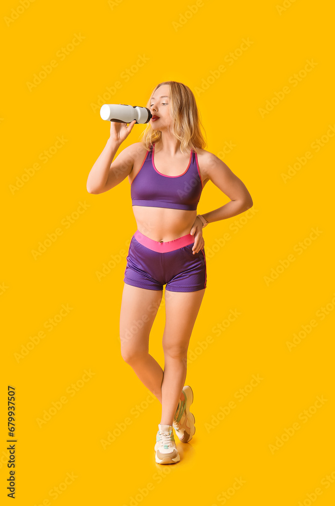 Beautiful sporty woman drinking water on yellow background. Weight loss concept
