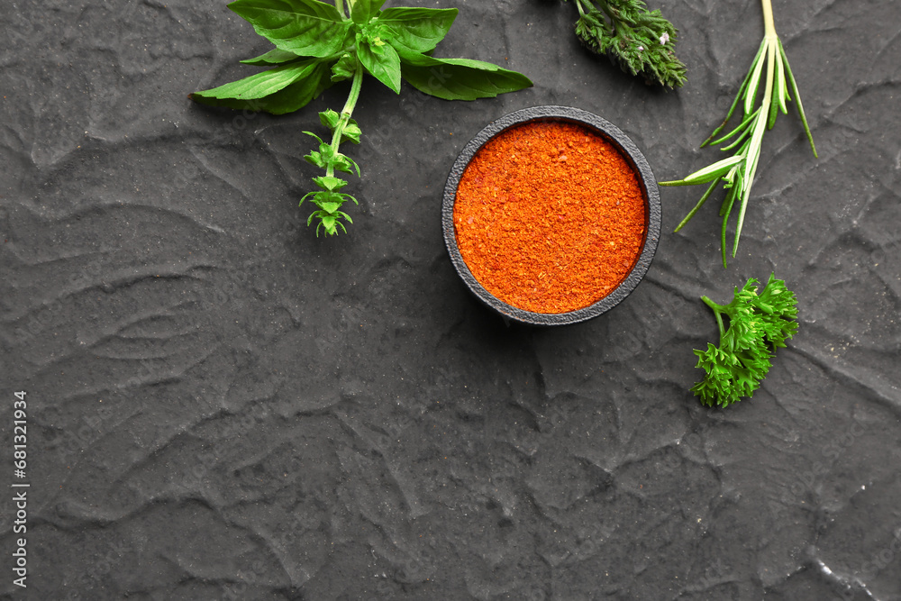 Composition with paprika powder and fresh herbs on dark background