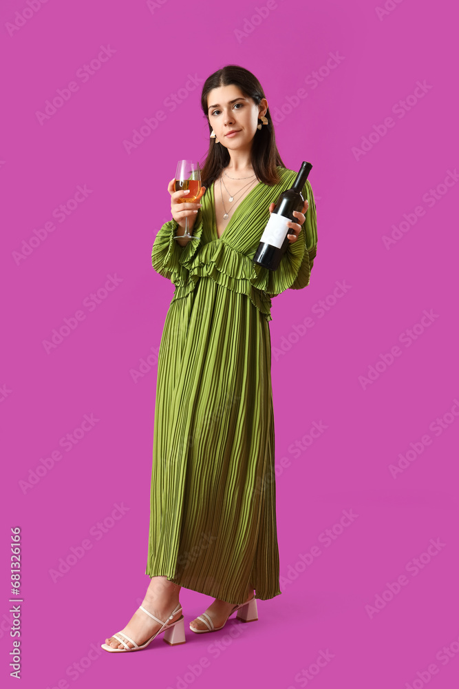 Young woman with glass and bottle of wine on purple background