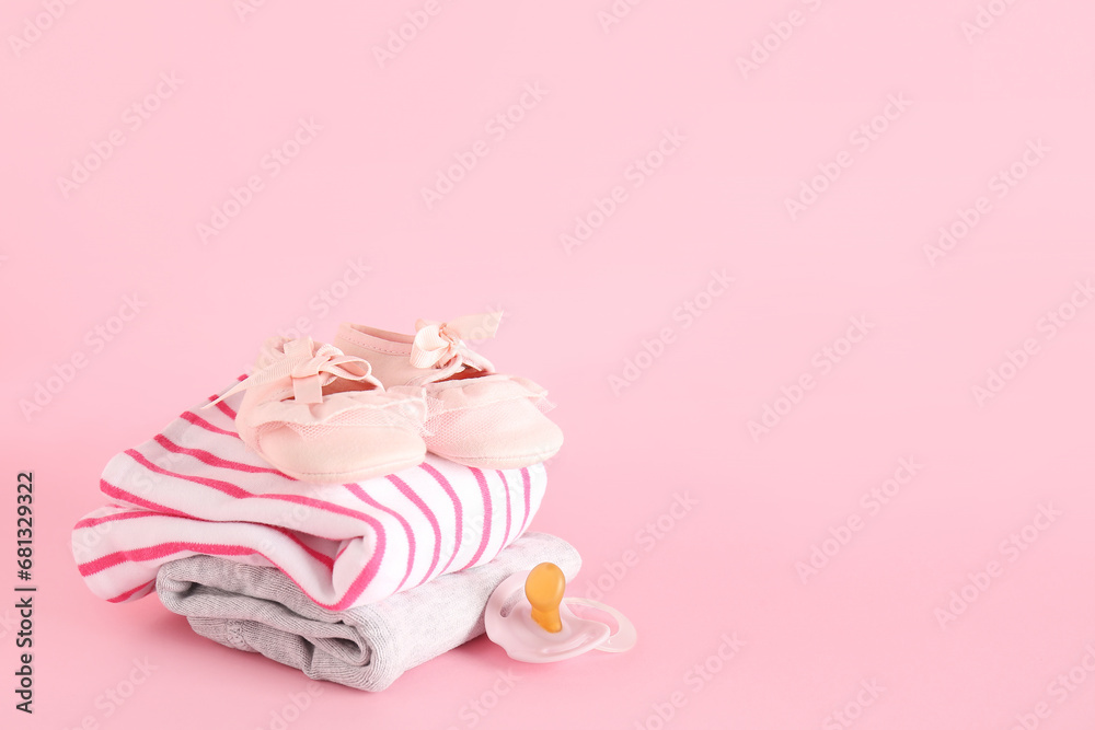 Stylish baby shoes with clothes and pacifier on pink background