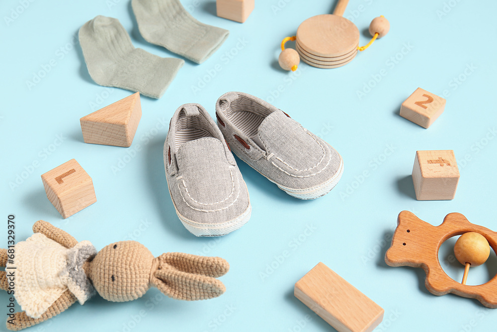 Stylish baby shoes with socks and different toys on blue background